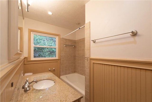 full bath featuring a textured ceiling, toilet, a wainscoted wall, vanity, and shower / bathing tub combination