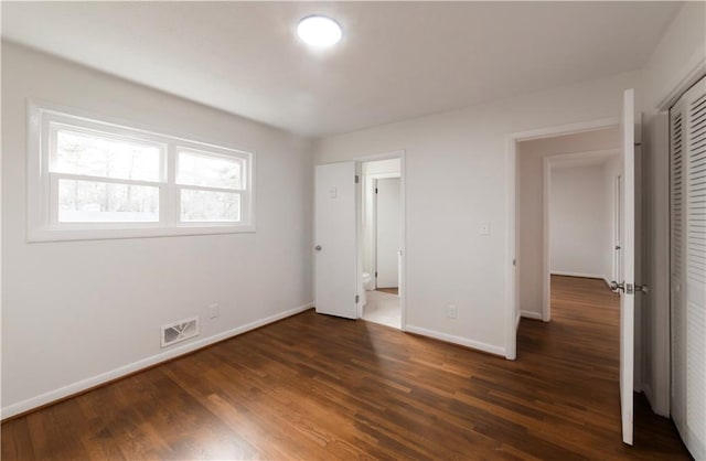 unfurnished bedroom with a closet, visible vents, dark wood finished floors, and baseboards