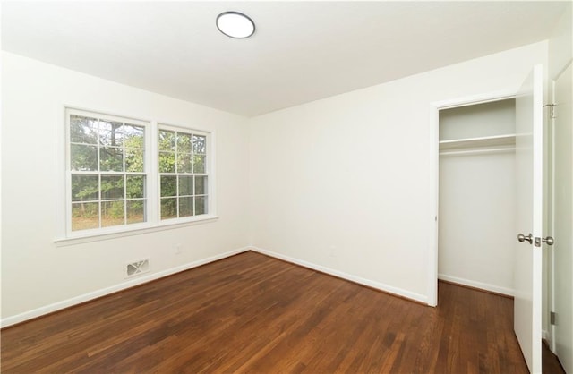unfurnished bedroom featuring dark wood-type flooring, a closet, visible vents, and baseboards