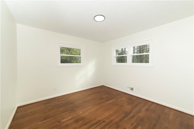 unfurnished room featuring dark wood-style flooring, visible vents, and baseboards