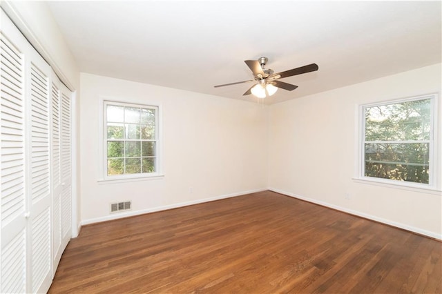 unfurnished bedroom with ceiling fan, dark wood-style flooring, visible vents, baseboards, and a closet
