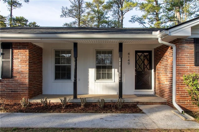view of exterior entry featuring covered porch and brick siding