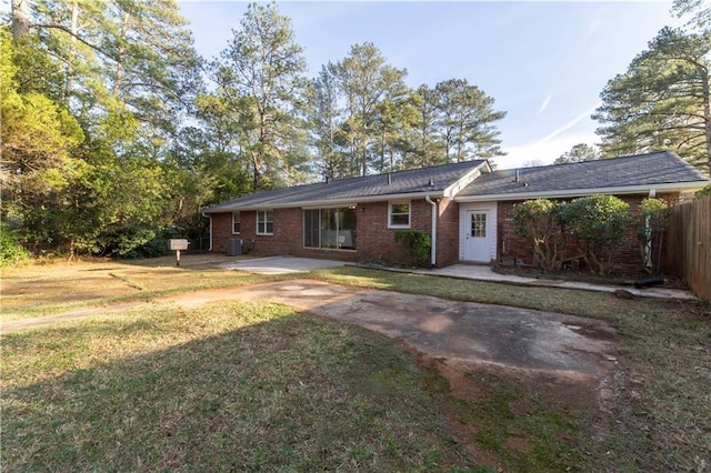 rear view of house with driveway, fence, cooling unit, a yard, and brick siding