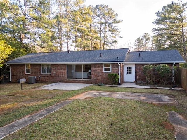 back of house featuring roof with shingles, brick siding, a patio, a lawn, and central AC unit