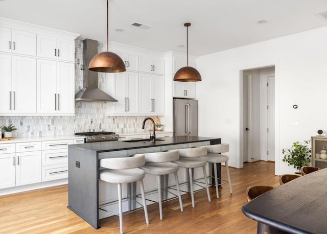 kitchen featuring tasteful backsplash, an island with sink, appliances with stainless steel finishes, wall chimney exhaust hood, and a sink