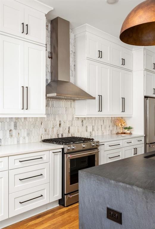 kitchen with backsplash, stainless steel appliances, wall chimney exhaust hood, white cabinets, and light wood finished floors