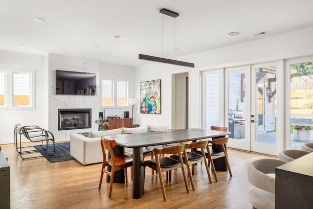 dining area with a high end fireplace, visible vents, light wood finished floors, and french doors