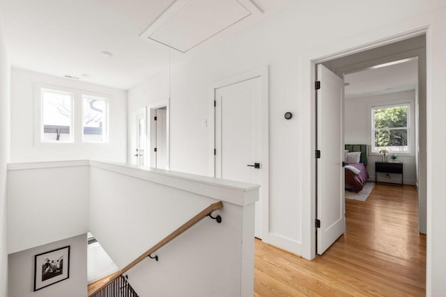 corridor featuring attic access, light wood-style flooring, an upstairs landing, and baseboards