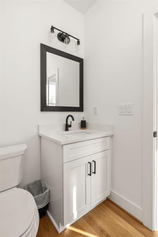 half bath featuring toilet, vanity, baseboards, and wood finished floors