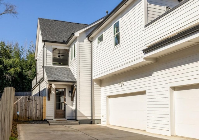 view of side of home with an attached garage, roof with shingles, and fence