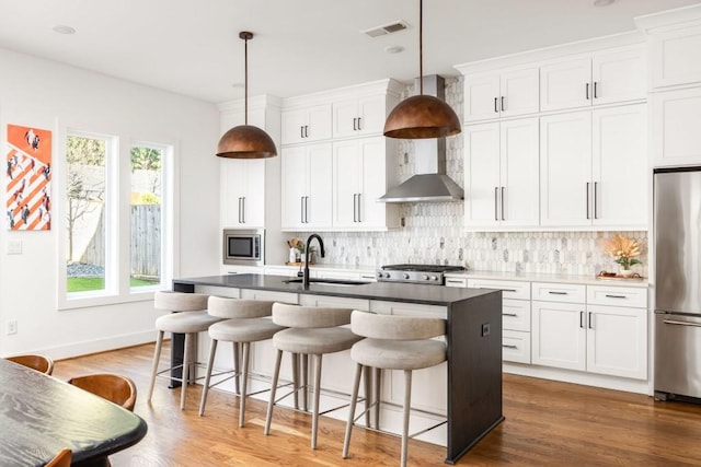 kitchen featuring visible vents, a kitchen island with sink, a sink, backsplash, and stainless steel appliances