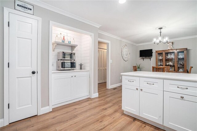 kitchen featuring white cabinetry, a chandelier, hanging light fixtures, ornamental molding, and light hardwood / wood-style floors