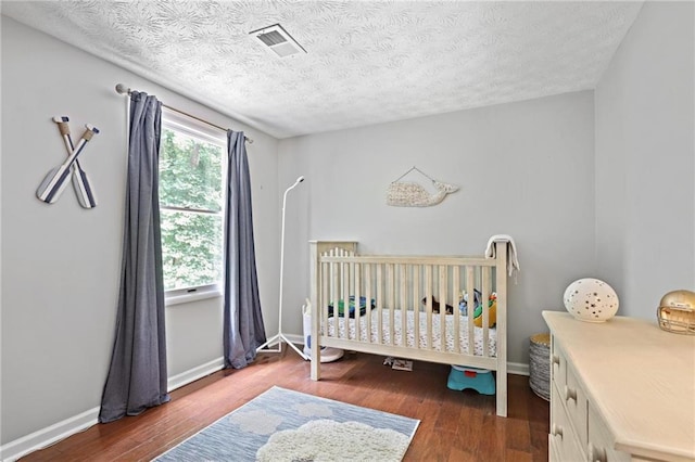 9470 Hillside Dr, Roswell, GA 30076 - bedroom with wood finished floors, a textured ceiling, and a crib
