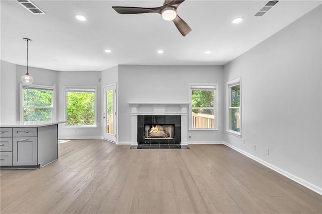 unfurnished living room featuring ceiling fan, a tile fireplace, and light hardwood / wood-style flooring