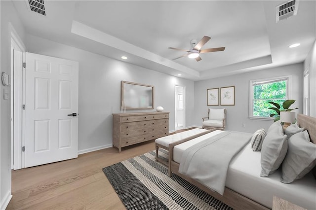 bedroom with ceiling fan, a raised ceiling, and light hardwood / wood-style flooring