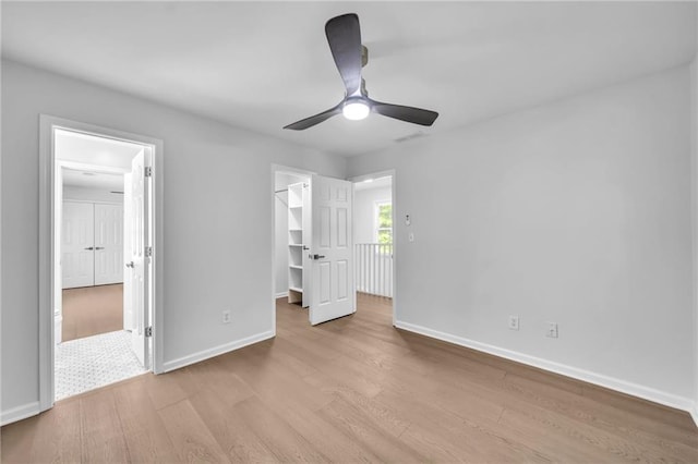 unfurnished bedroom with ceiling fan, a closet, a spacious closet, and light hardwood / wood-style flooring