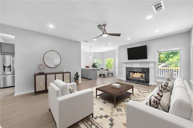 living room with a tile fireplace, light wood-type flooring, plenty of natural light, and ceiling fan