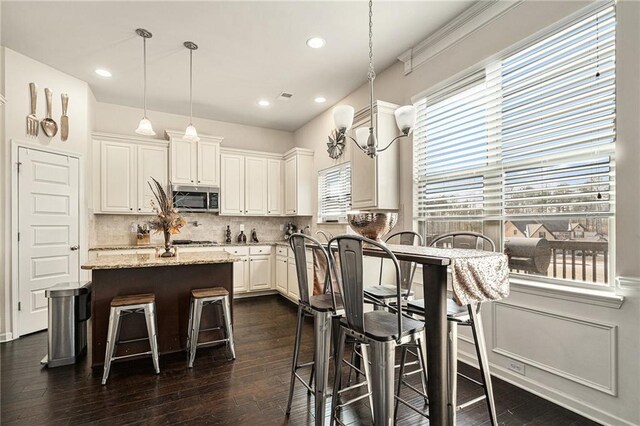 kitchen with light stone counters, pendant lighting, a center island, backsplash, and white cabinetry