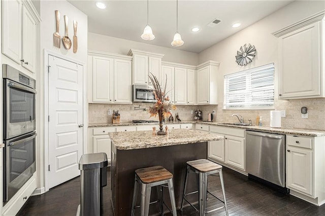 kitchen with stainless steel appliances, sink, a center island, white cabinetry, and light stone countertops