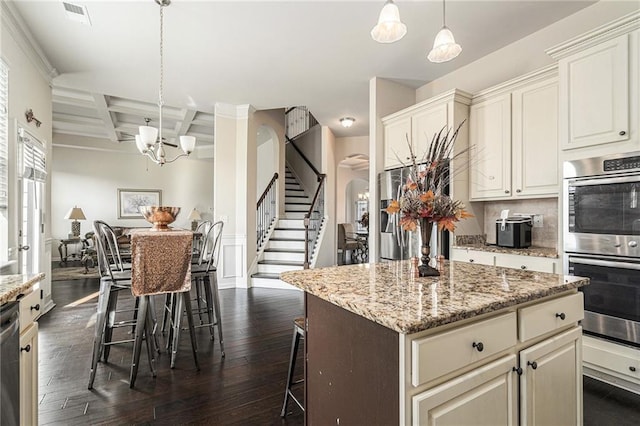 kitchen with coffered ceiling, hanging light fixtures, beam ceiling, appliances with stainless steel finishes, and a kitchen breakfast bar