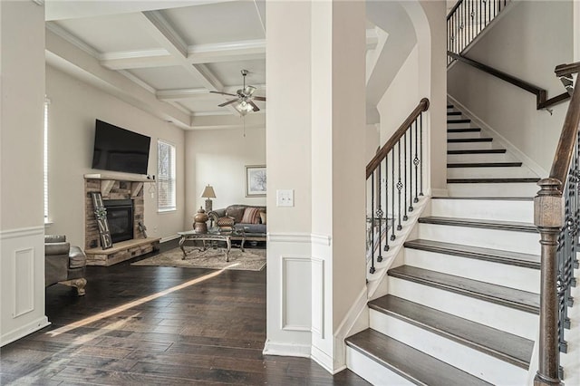 staircase featuring a stone fireplace, hardwood / wood-style floors, ceiling fan, coffered ceiling, and beam ceiling