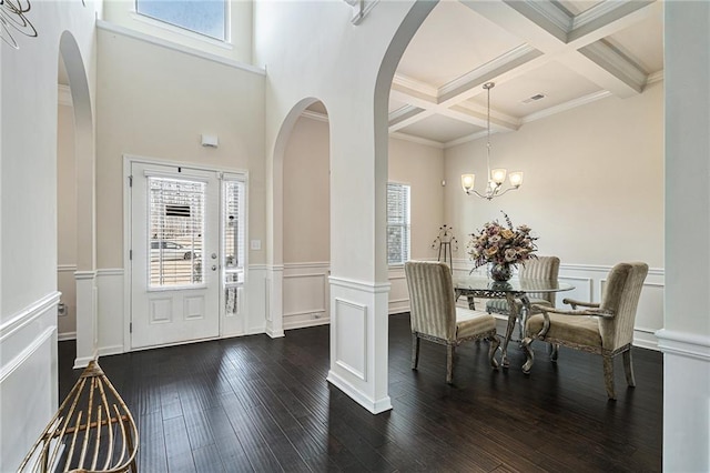 entrance foyer with ornamental molding, coffered ceiling, dark hardwood / wood-style flooring, a notable chandelier, and beam ceiling