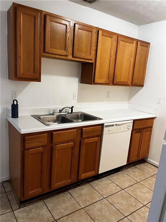 kitchen with sink, dishwasher, a textured ceiling, and light tile patterned floors