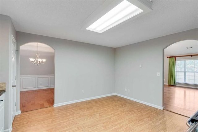 1227 Casper Ln, Winder, GA 30680 - empty room with arched walkways, light wood-type flooring, a chandelier, and a textured ceiling