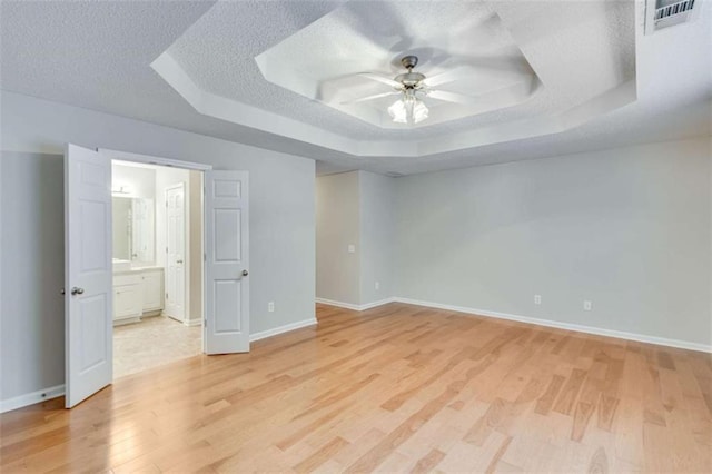 1227 Casper Ln, Winder, GA 30680 - unfurnished bedroom featuring a tray ceiling, light wood-type flooring, baseboards, a textured ceiling, and ensuite bath