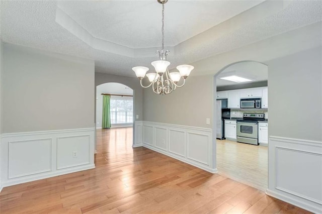 1227 Casper Ln, Winder, GA 30680 - unfurnished dining area with arched walkways, a raised ceiling, a decorative wall, light wood-style floors, and a chandelier