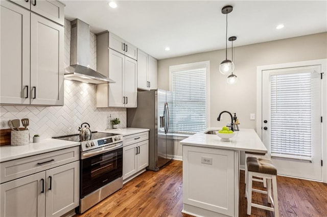 kitchen featuring appliances with stainless steel finishes, a breakfast bar, sink, a kitchen island with sink, and wall chimney exhaust hood