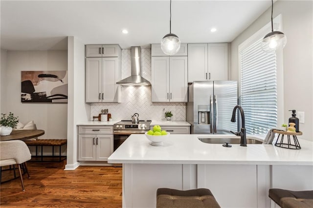 kitchen featuring pendant lighting, tasteful backsplash, a breakfast bar area, stainless steel appliances, and wall chimney range hood