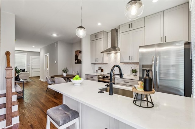 kitchen featuring appliances with stainless steel finishes, a breakfast bar, decorative backsplash, hanging light fixtures, and wall chimney range hood