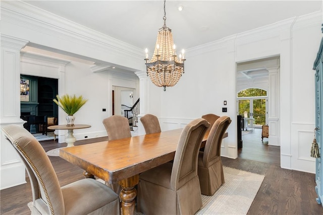 dining space featuring ornamental molding, wood finished floors, ornate columns, a decorative wall, and a notable chandelier