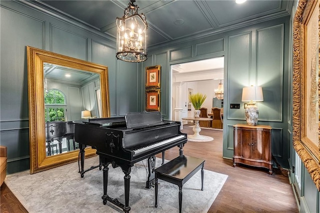 sitting room with a notable chandelier, a decorative wall, coffered ceiling, wood finished floors, and ornamental molding