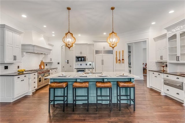 kitchen with a kitchen bar, custom range hood, white cabinets, and built in appliances