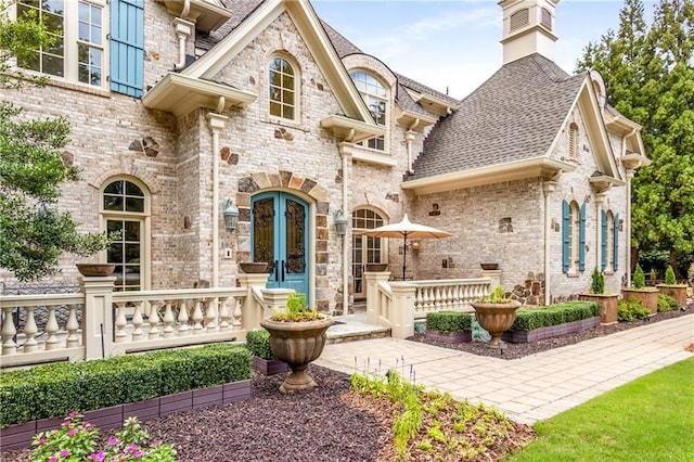 doorway to property with french doors, brick siding, and roof with shingles