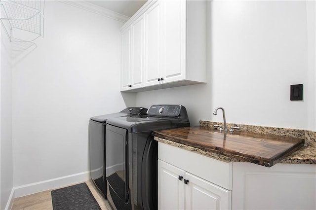 laundry room with washing machine and clothes dryer, cabinet space, light wood-style flooring, ornamental molding, and baseboards