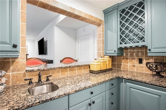 kitchen with a sink, crown molding, dark stone countertops, and backsplash