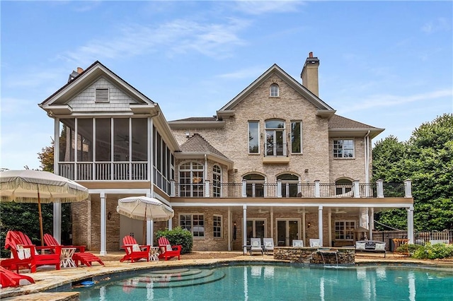 back of house featuring a sunroom, a chimney, a patio area, and a balcony