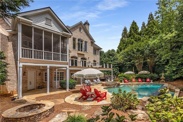 back of property with a patio area, an outdoor fire pit, a chimney, and a sunroom