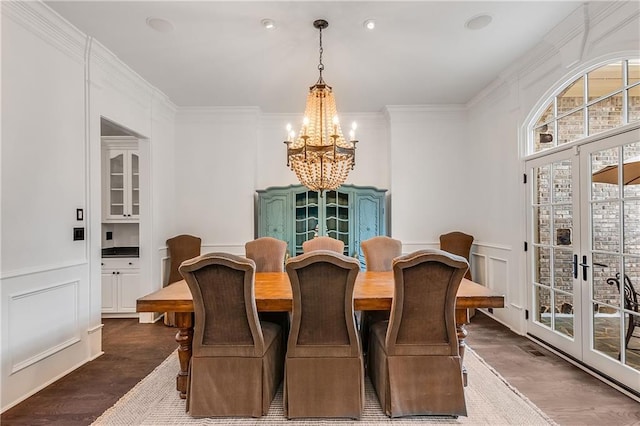 dining room with wainscoting, dark wood-style floors, crown molding, a chandelier, and a decorative wall