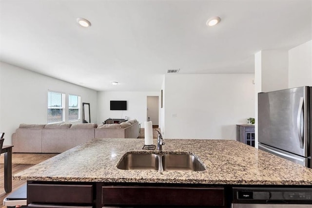 kitchen featuring a center island with sink, freestanding refrigerator, dark brown cabinetry, a sink, and dishwasher