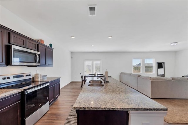 kitchen with wood finished floors, a sink, visible vents, appliances with stainless steel finishes, and light stone countertops