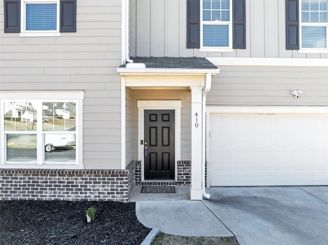 doorway to property featuring an attached garage, driveway, board and batten siding, and brick siding