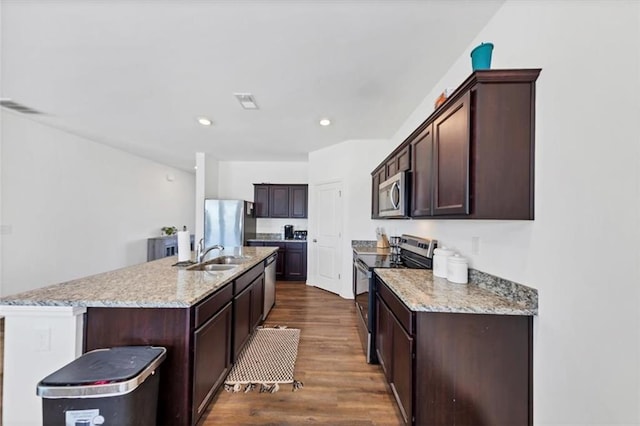 kitchen featuring dark wood finished floors, appliances with stainless steel finishes, a sink, dark brown cabinetry, and an island with sink