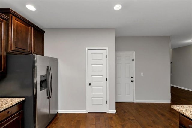 kitchen with dark brown cabinetry, light stone countertops, dark hardwood / wood-style floors, and stainless steel refrigerator with ice dispenser