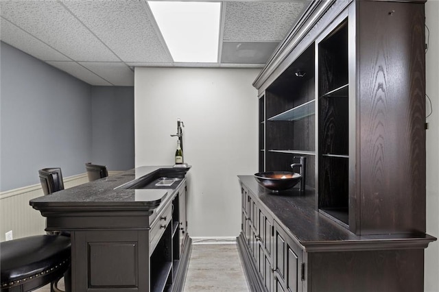 kitchen featuring kitchen peninsula, a drop ceiling, a breakfast bar, sink, and light hardwood / wood-style floors