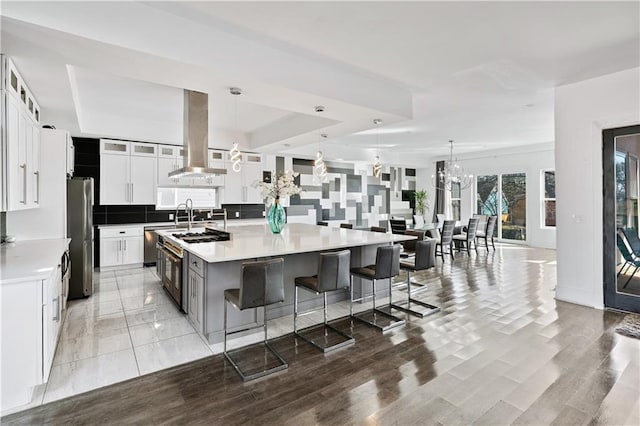 kitchen with decorative backsplash, a large island with sink, appliances with stainless steel finishes, an inviting chandelier, and island range hood