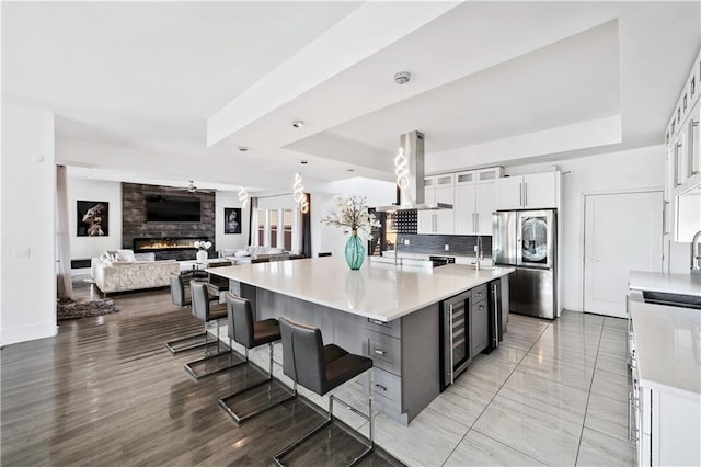 kitchen featuring beverage cooler, a tray ceiling, island exhaust hood, smart refrigerator, and a large fireplace